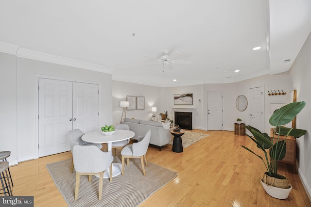 dining area featuring ceiling fan, a fireplace, light wood-style floors, crown molding, and recessed lighting