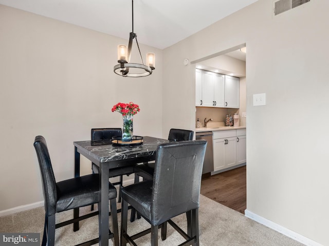 carpeted dining room with a chandelier, baseboards, and a sink