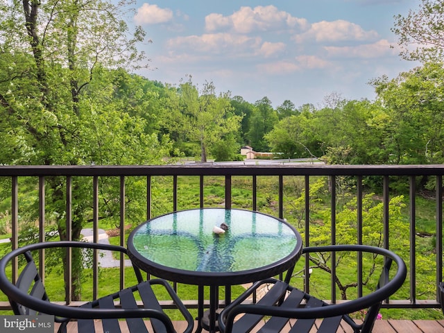 balcony featuring outdoor dining area and a wooded view