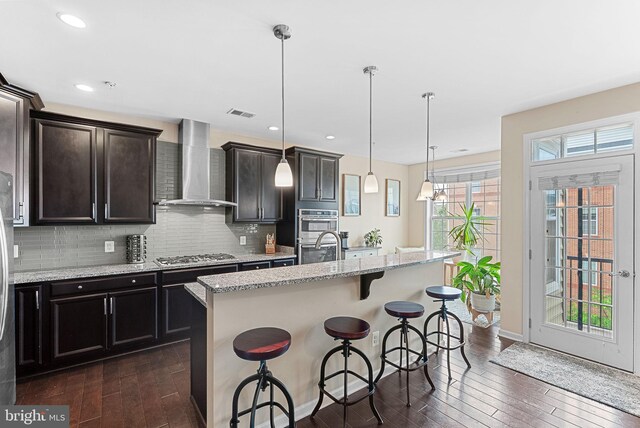 23483 Aldie Manor Ter, Ashburn, VA 20148 - kitchen with wall chimney exhaust hood, appliances with stainless steel finishes, dark wood finished floors, a kitchen breakfast bar, and tasteful backsplash