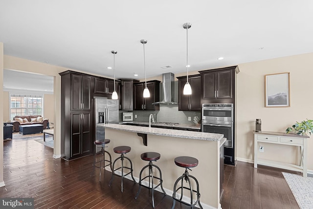 23483 Aldie Manor Ter, Ashburn, VA 20148 - kitchen with wall chimney range hood, stainless steel appliances, dark brown cabinetry, a breakfast bar, and recessed lighting