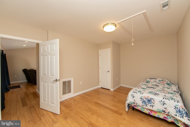 bedroom with attic access, light wood-style floors, and baseboards