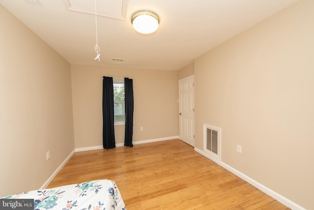 bedroom with light wood-style floors, baseboards, and attic access