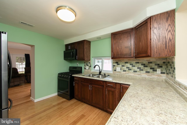 kitchen with stainless steel appliances, a sink, light countertops, light wood finished floors, and backsplash