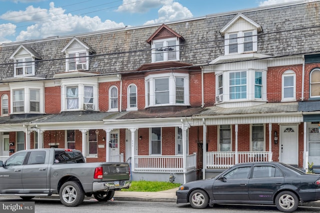 townhome / multi-family property featuring covered porch, brick siding, and cooling unit