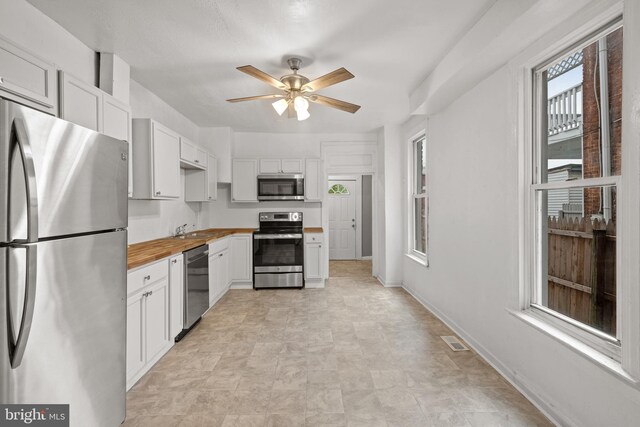 kitchen with stainless steel appliances, butcher block counters, ceiling fan, a sink, and white cabinetry