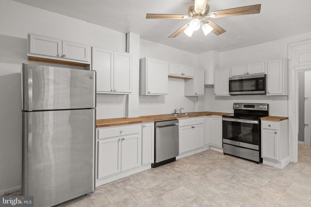 kitchen with appliances with stainless steel finishes, wood counters, a sink, ceiling fan, and white cabinets