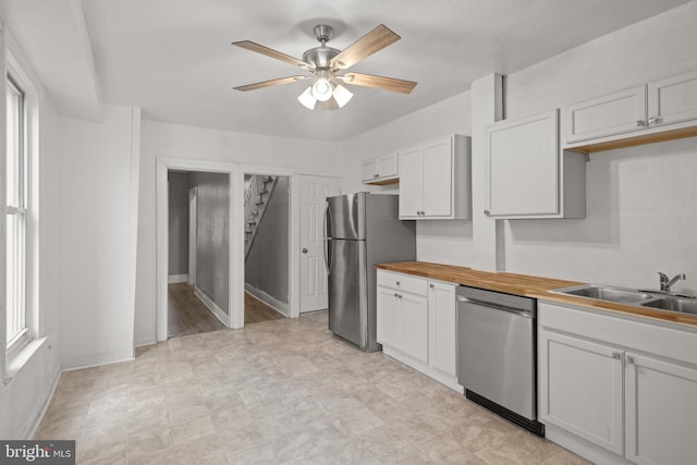 kitchen with stainless steel appliances, wooden counters, ceiling fan, white cabinets, and a sink