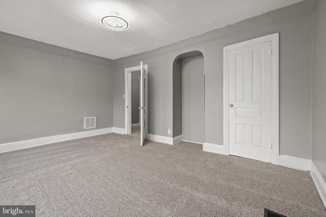 carpeted empty room featuring arched walkways and baseboards