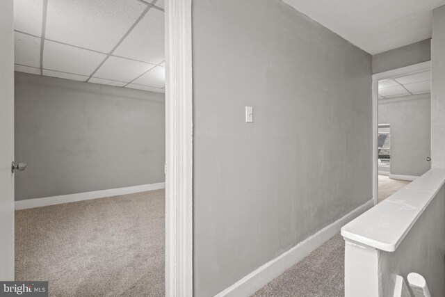 hallway featuring carpet, baseboards, and a paneled ceiling