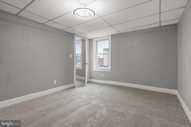 carpeted empty room featuring a paneled ceiling and baseboards