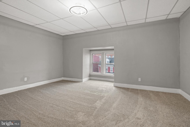 carpeted empty room featuring a drop ceiling and baseboards