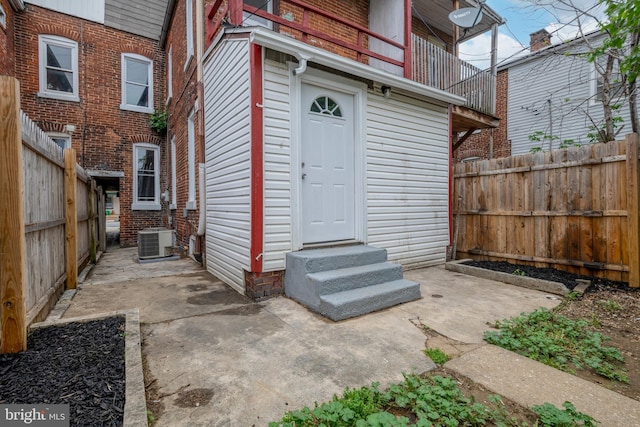 view of exterior entry with central AC, fence, and a patio