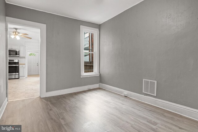 empty room with light wood-style floors, a ceiling fan, and baseboards