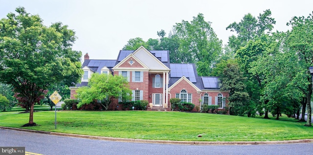 colonial-style house featuring roof mounted solar panels, a front yard, and brick siding