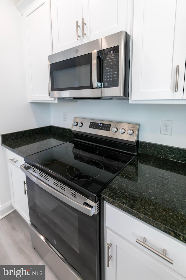 93 6th St W, Laurel, DE 19956 - kitchen featuring appliances with stainless steel finishes, white cabinets, light wood-type flooring, and dark stone countertops