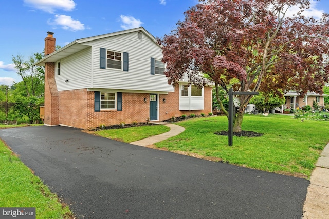 tri-level home featuring a chimney, brick siding, a front lawn, and driveway