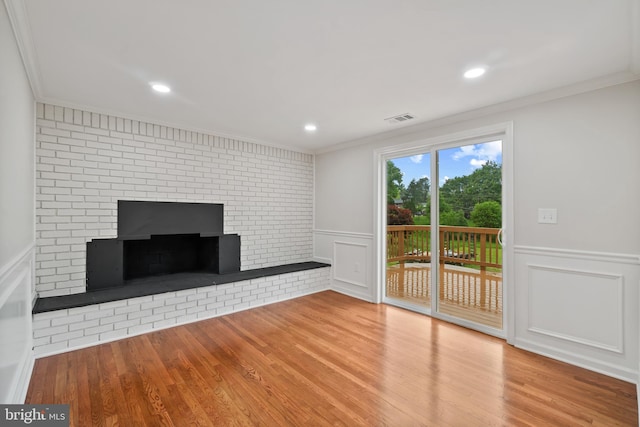 unfurnished living room with crown molding, a decorative wall, wood finished floors, a brick fireplace, and recessed lighting