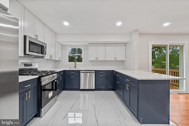 kitchen featuring appliances with stainless steel finishes, a peninsula, white cabinets, blue cabinetry, and recessed lighting