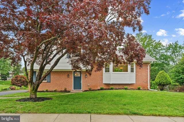 view of property hidden behind natural elements with a front yard and brick siding