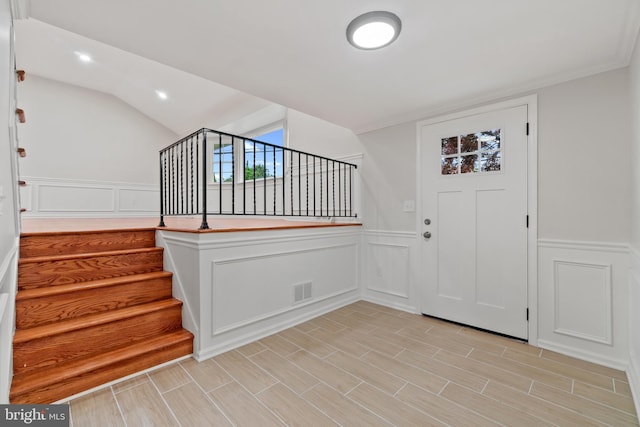foyer entrance featuring stairs, a decorative wall, and wainscoting