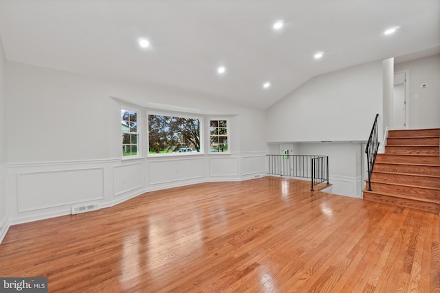 empty room with a decorative wall, wood finished floors, wainscoting, vaulted ceiling, and recessed lighting