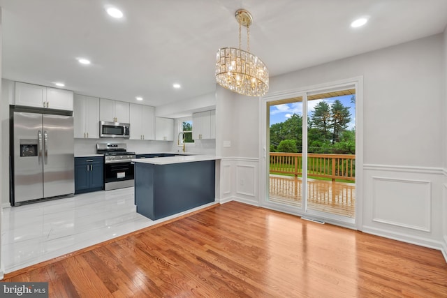 kitchen with appliances with stainless steel finishes, a decorative wall, a peninsula, a sink, and light countertops