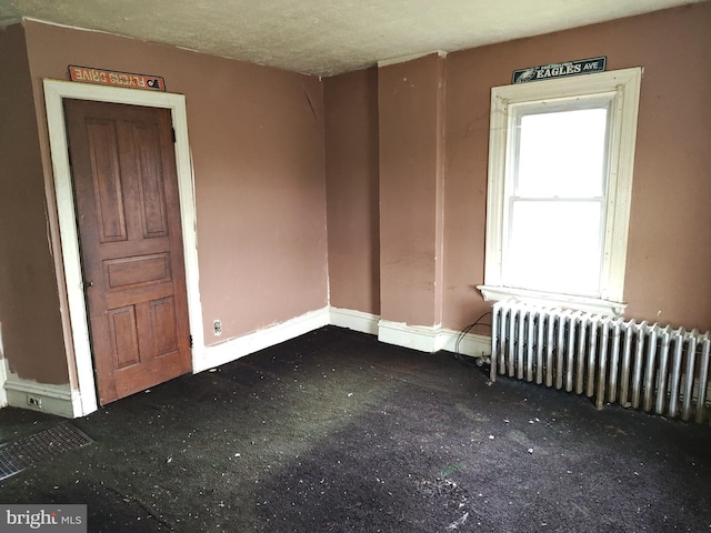 carpeted empty room featuring radiator and baseboards