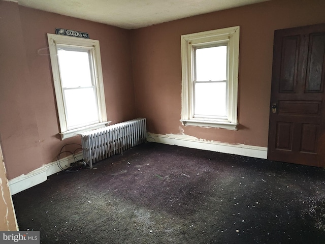 carpeted empty room with radiator and baseboards