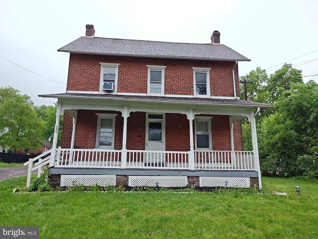 view of front of house with a chimney, brick siding, a porch, and a front yard