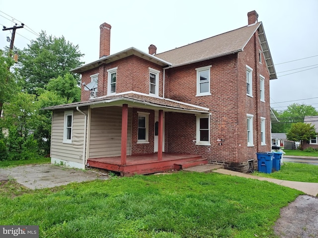 rear view of house with covered porch, a chimney, a lawn, brick siding, and a shingled roof