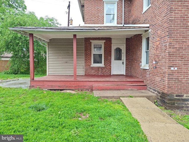 view of exterior entry featuring covered porch, brick siding, and a yard