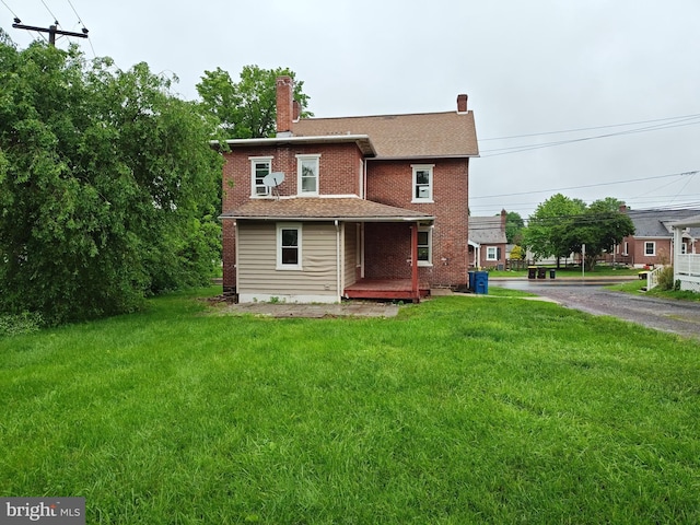 rear view of property featuring a porch, a lawn, brick siding, and a chimney