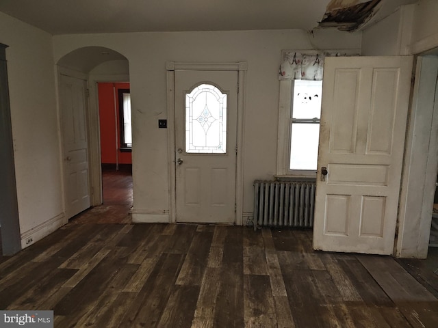 foyer with radiator heating unit, arched walkways, and dark wood-style flooring