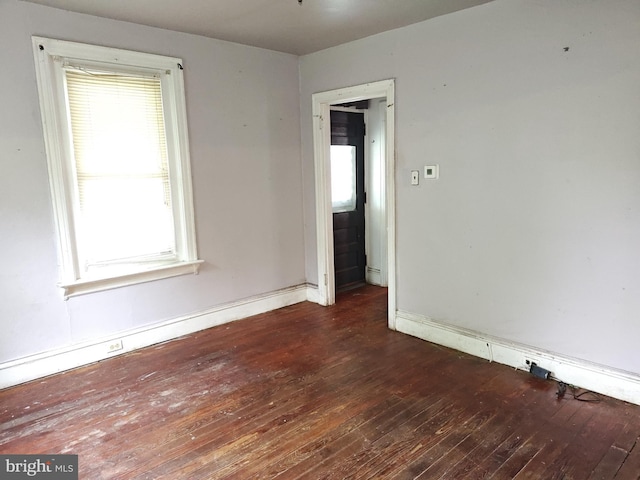 unfurnished room featuring dark wood-type flooring, healthy amount of natural light, and baseboards