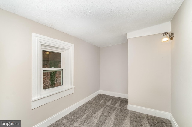 unfurnished room with dark colored carpet, baseboards, and a textured ceiling
