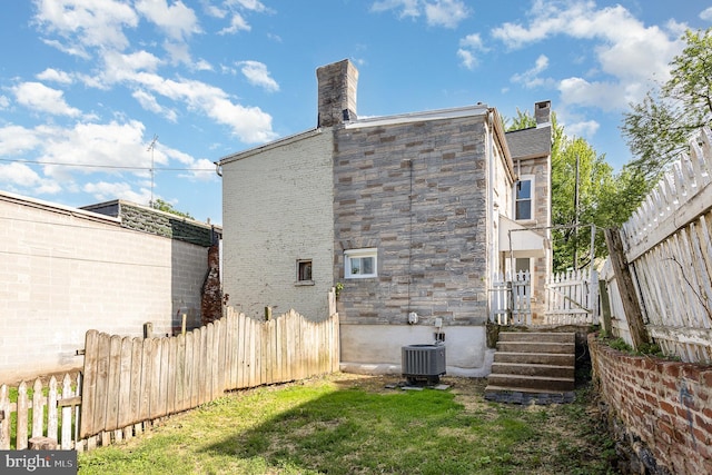 back of house featuring fence, a chimney, and central AC unit
