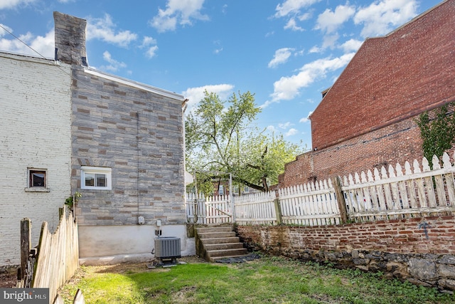 view of side of home featuring fence, cooling unit, and stone siding
