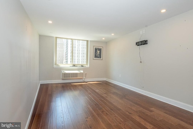 unfurnished room featuring dark wood finished floors, baseboards, recessed lighting, and an AC wall unit