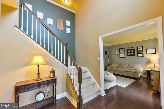 stairs featuring hardwood / wood-style floors, baseboards, ornamental molding, and a towering ceiling
