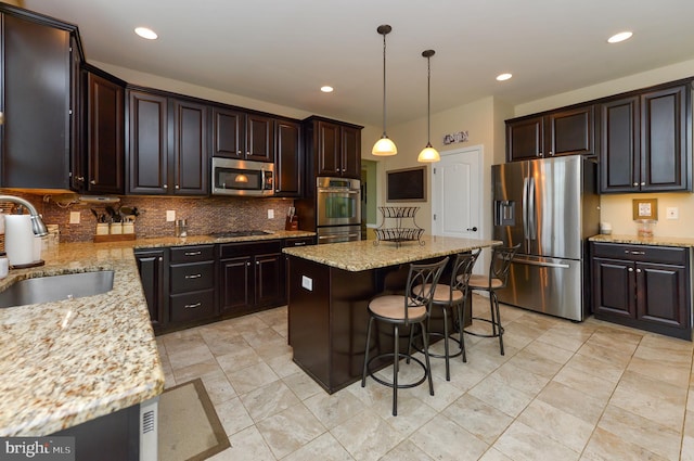 kitchen with appliances with stainless steel finishes, a sink, backsplash, a kitchen bar, and light stone countertops