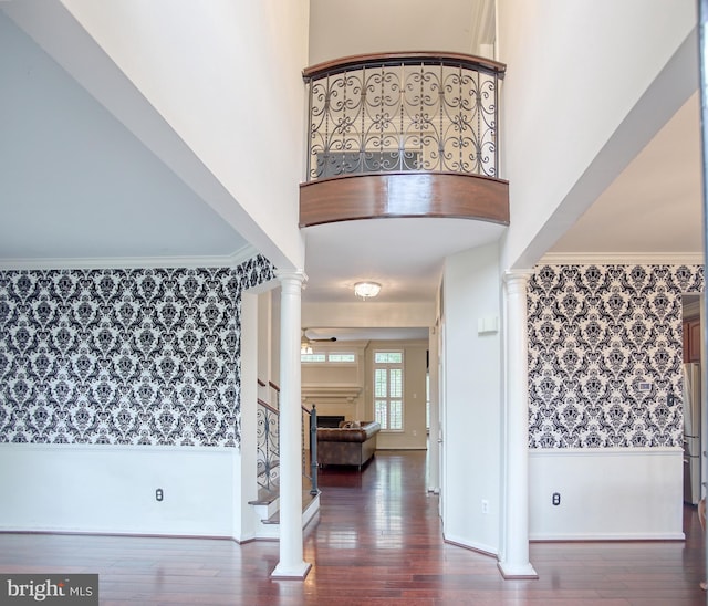 entrance foyer featuring wallpapered walls, decorative columns, wainscoting, wood finished floors, and baseboards