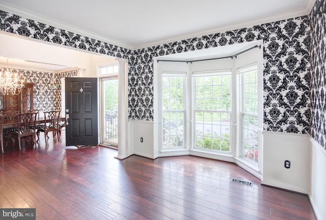 unfurnished dining area featuring wallpapered walls, a chandelier, a wainscoted wall, hardwood / wood-style floors, and crown molding