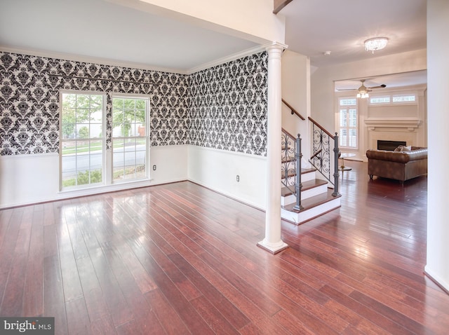 unfurnished room with wallpapered walls, a wainscoted wall, ceiling fan, a fireplace, and stairs