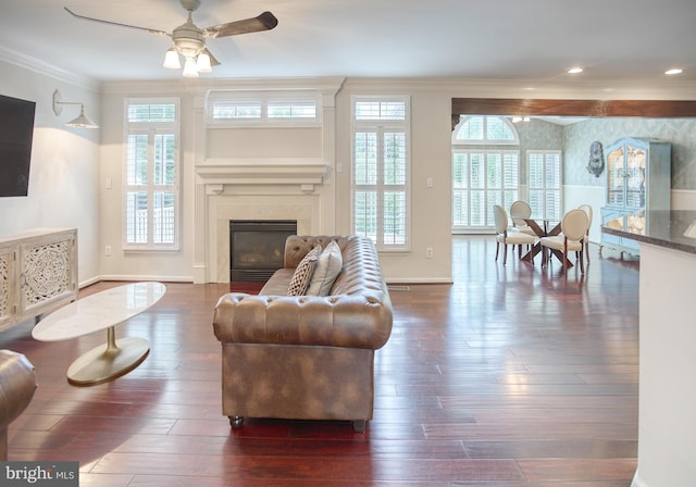 living room featuring dark wood-style flooring, a ceiling fan, crown molding, a premium fireplace, and baseboards