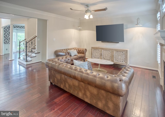 living area with dark wood finished floors, ceiling fan, stairs, ornamental molding, and a fireplace
