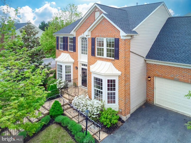 view of front of property with a shingled roof, brick siding, driveway, and an attached garage