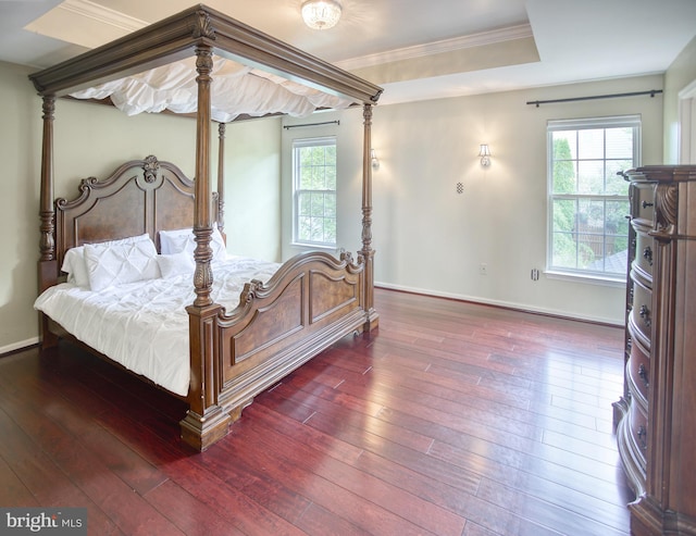 bedroom featuring wood-type flooring, baseboards, crown molding, and a tray ceiling