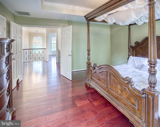 bedroom featuring a chandelier, dark wood finished floors, baseboards, ornamental molding, and a tray ceiling