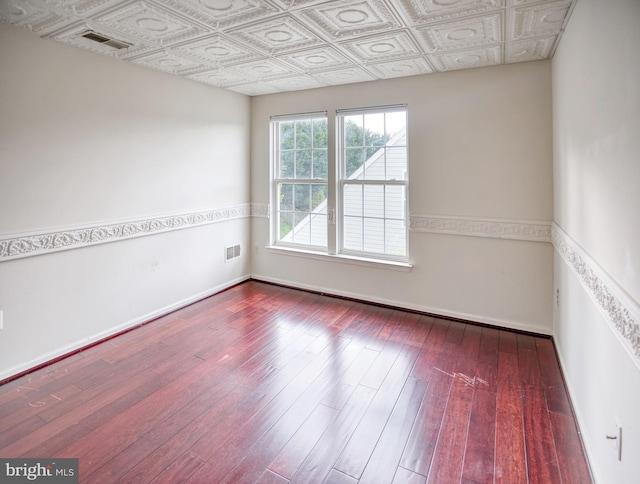 empty room with an ornate ceiling, hardwood / wood-style floors, and baseboards